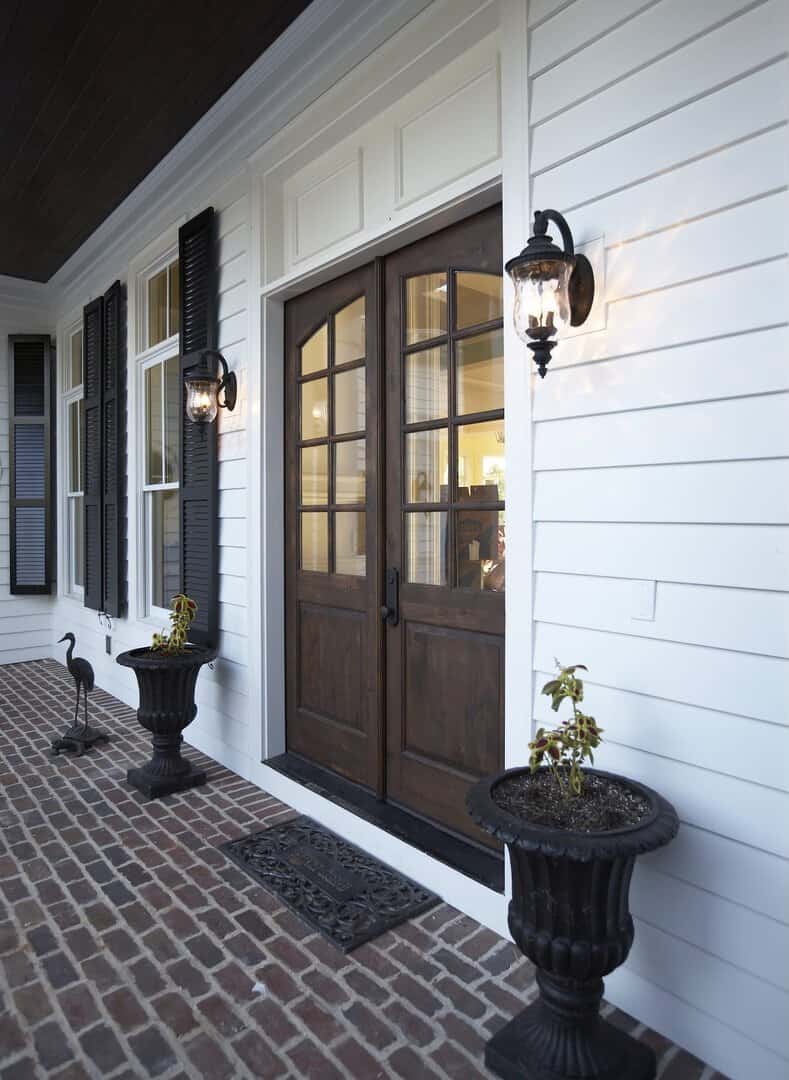Front porch with white siding, black shutters, and wooden door with glass panes.